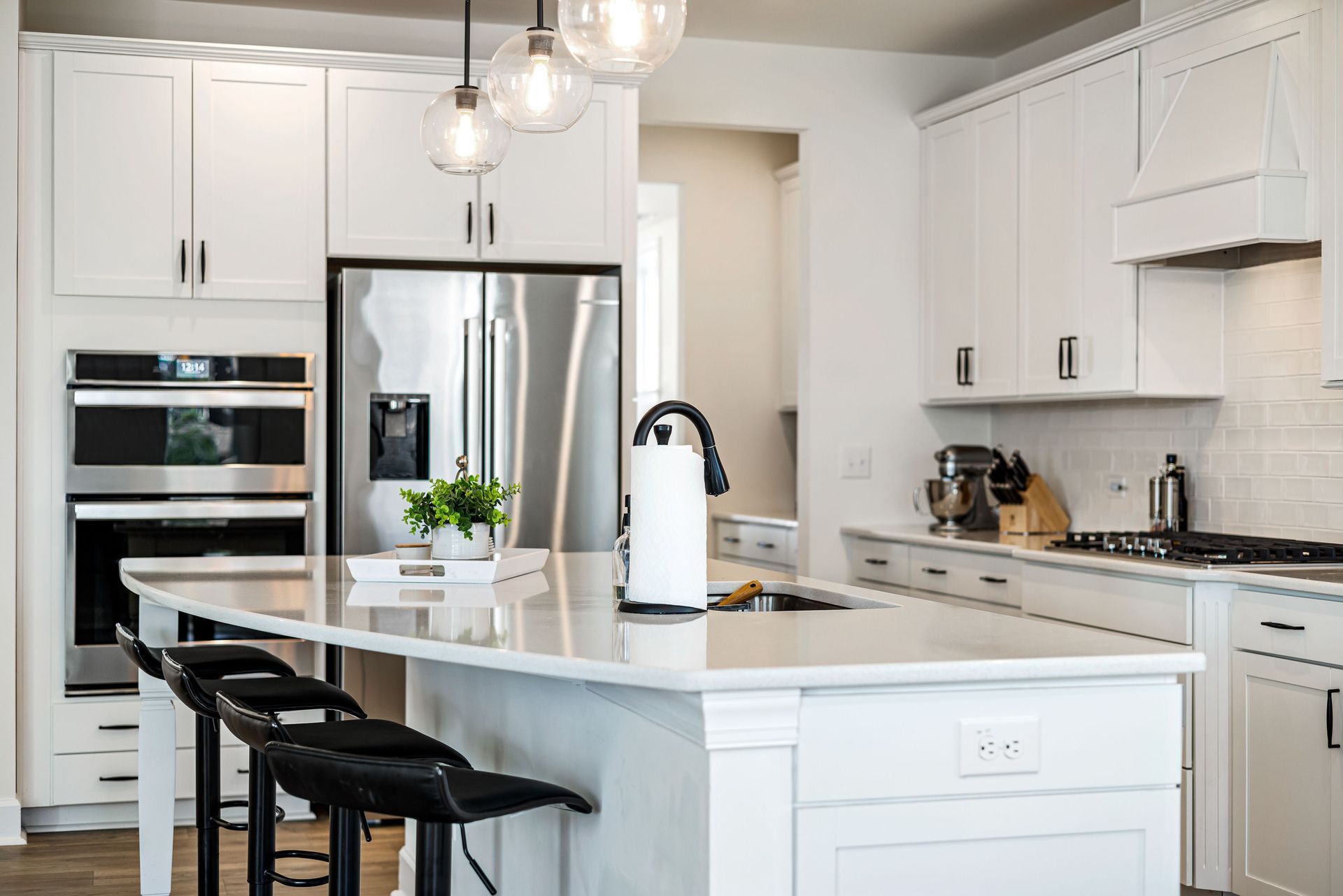 Bright white modern kitchen with island, bar stools, stainless appliances, and pendant lights
