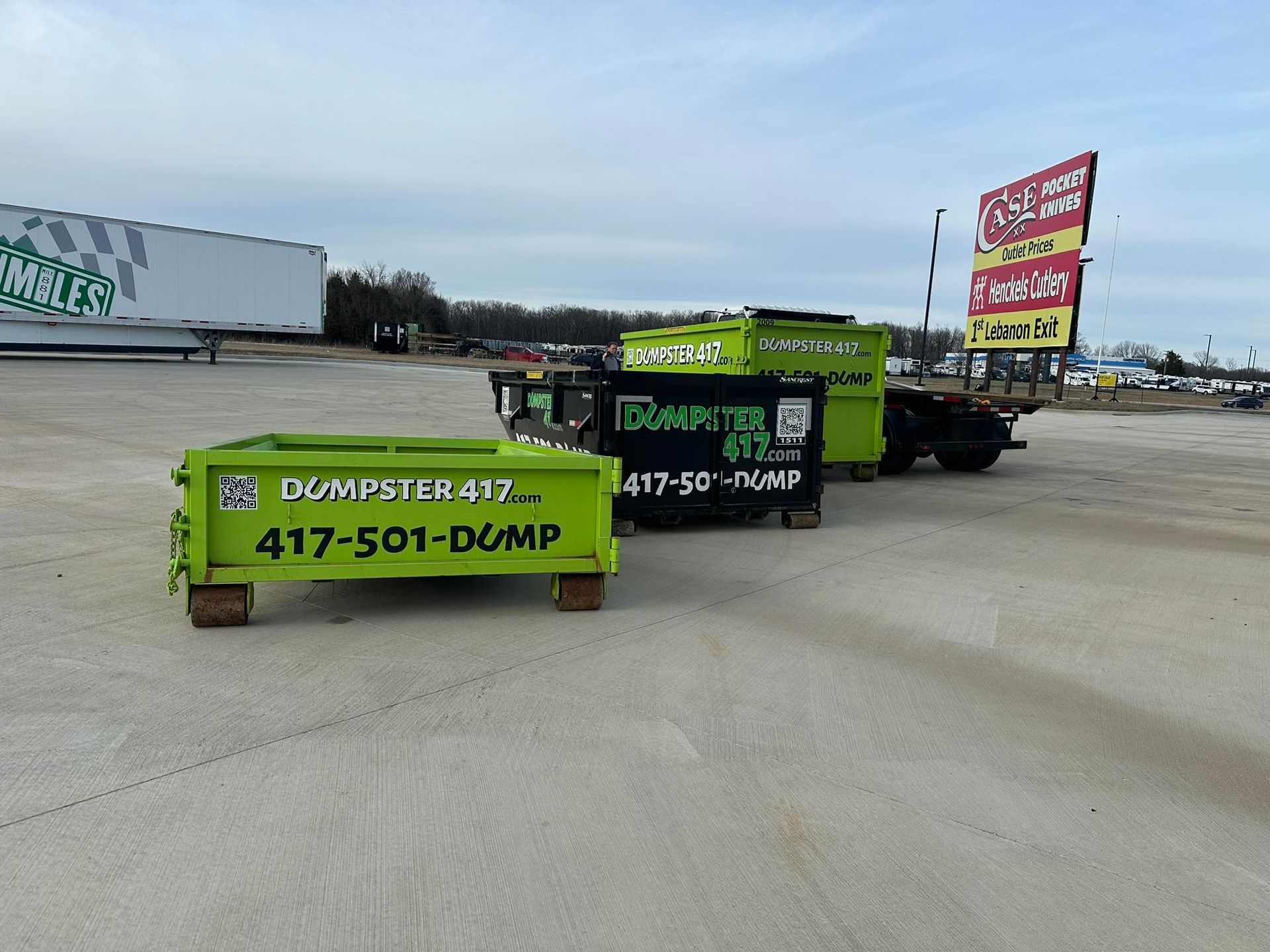 Bright green dumpsters and trucks in a parking lot, advertising a local dump service.