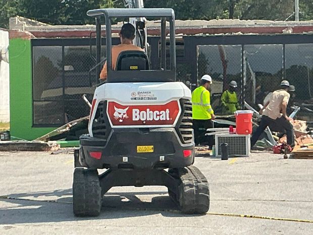 Bobcat loader at a construction site with workers around a building under repair