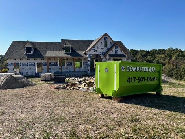 Green dumpster in front of a house under construction on a sunny day