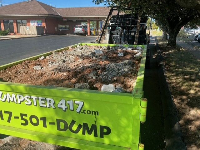 Bright green dumpster filled with debris parked outside a strip mall in a parking lot
