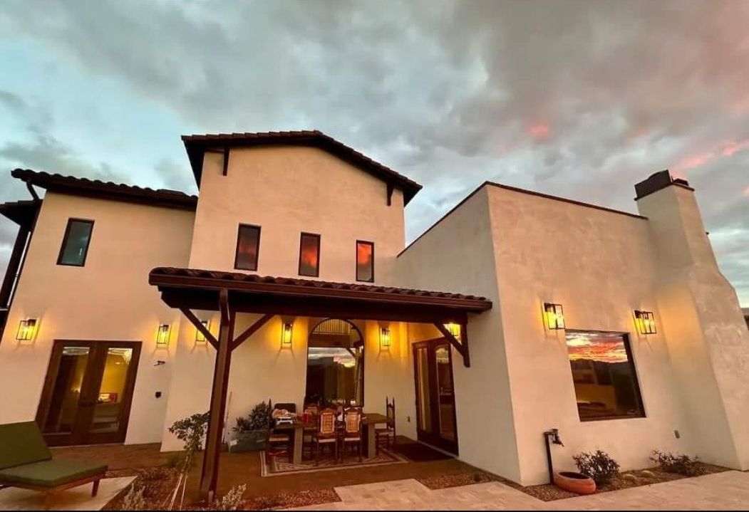 Back patio of a stucco home with a pergola and dining table at sunset.