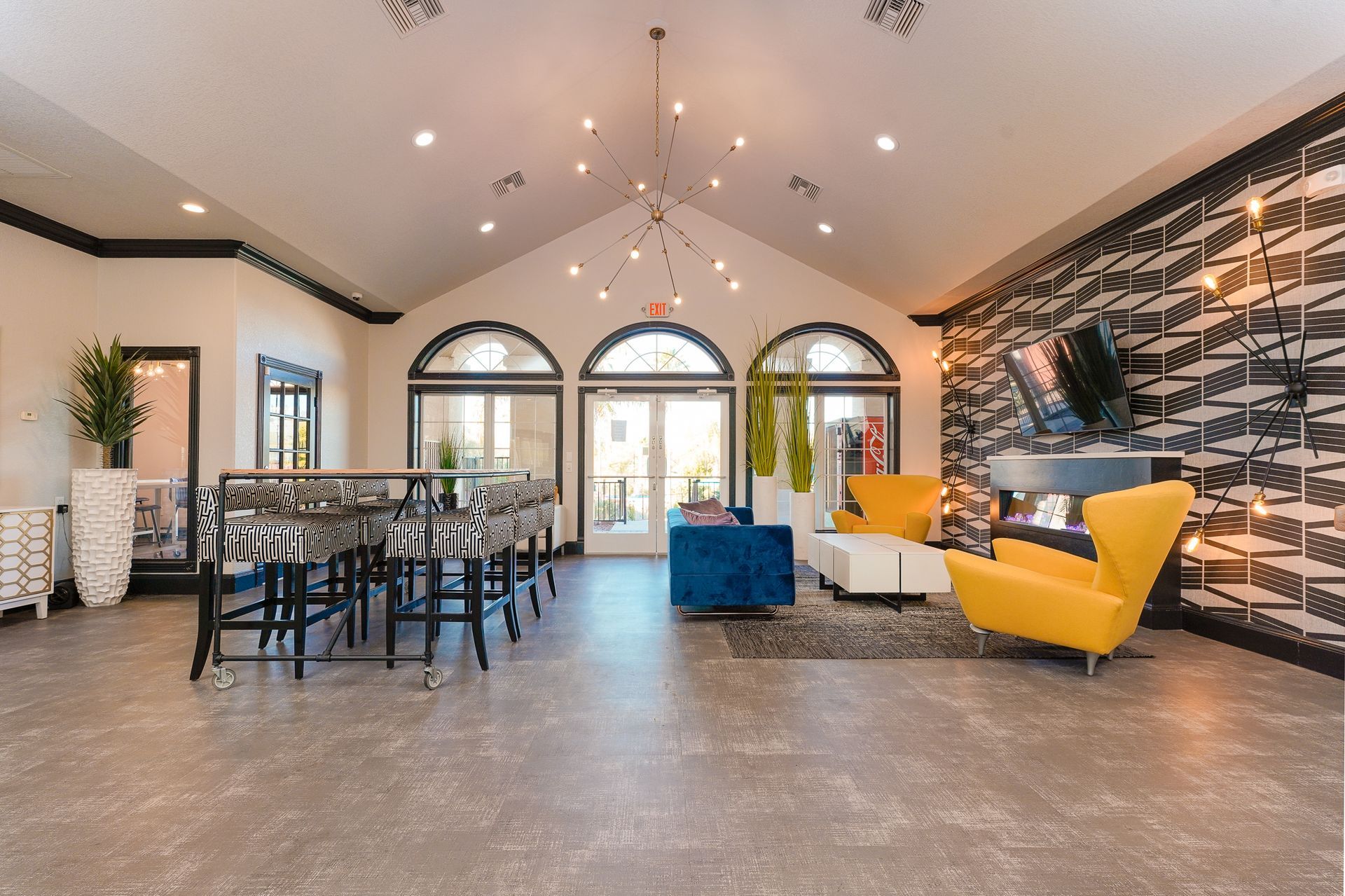 Lounge area with high ceilings, a table with chairs, colorful seating, and patterned accent wall.