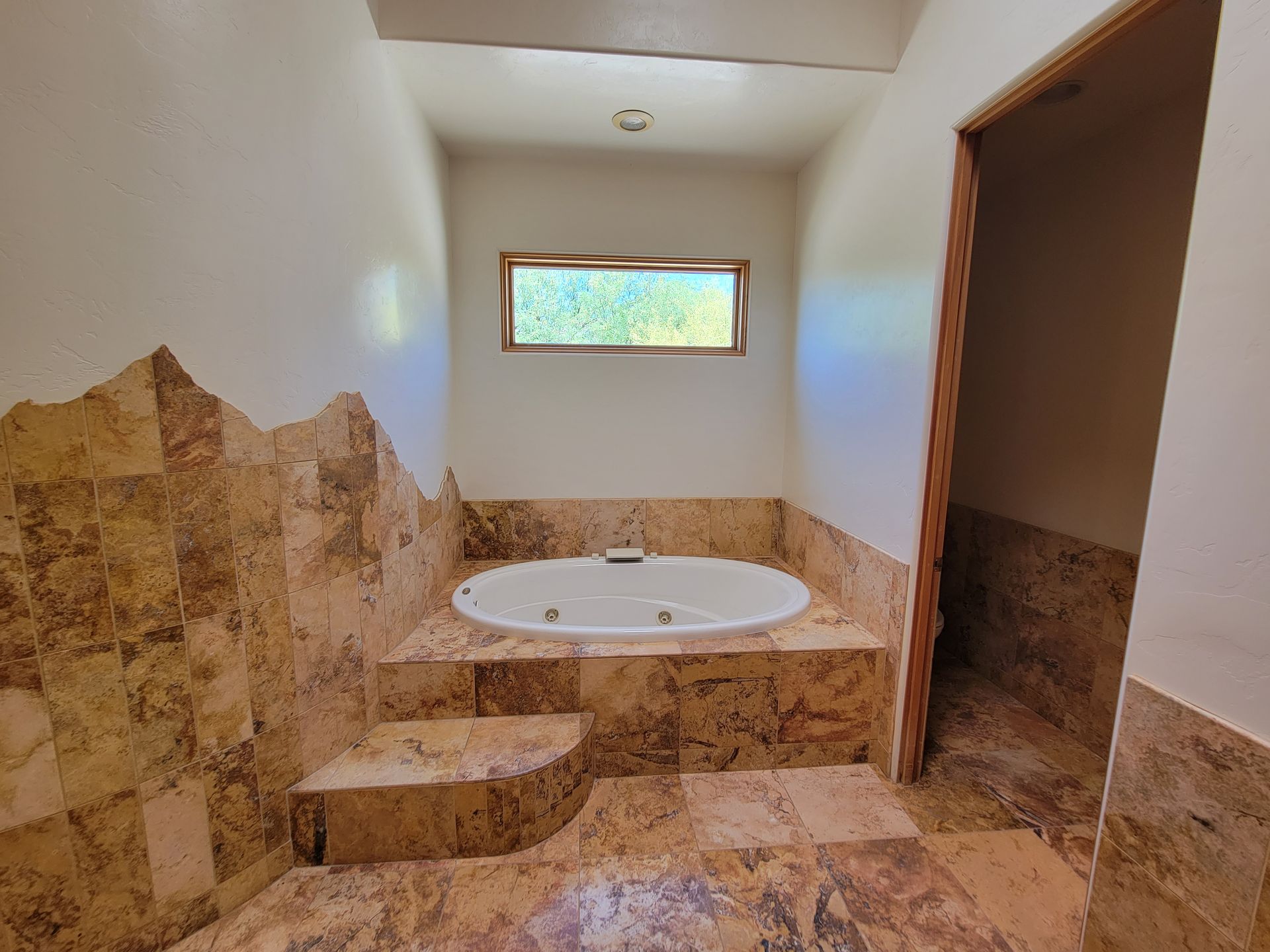 Bathroom with a raised jacuzzi tub. Tiled surfaces, small window, and open doorway on the right.
