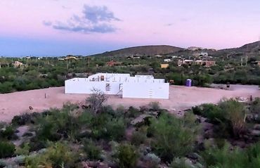 White building under construction in a desert landscape with purple and pink sky.