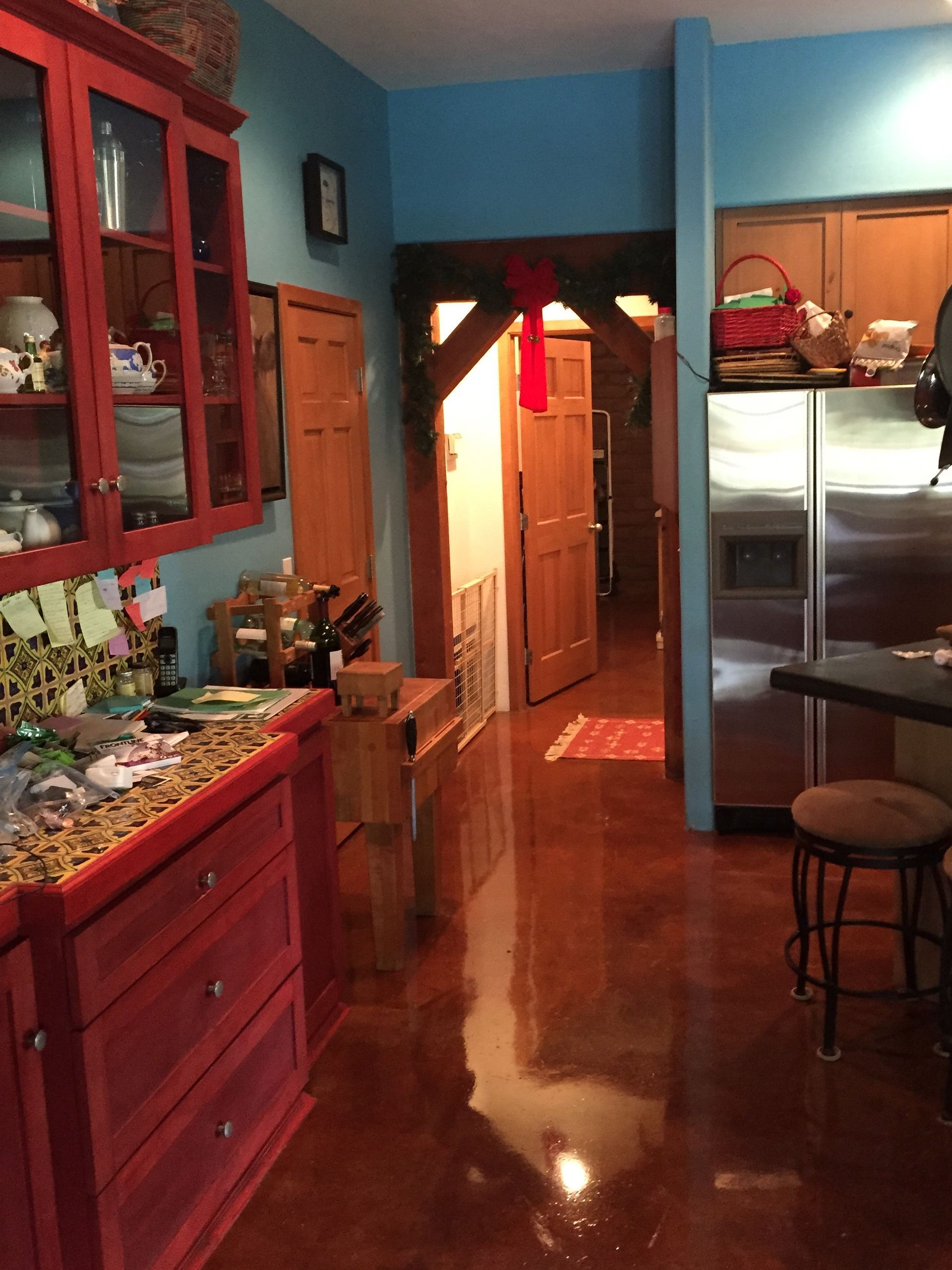 Red cabinets, blue walls, brown floor in a kitchen with a view into hallway.