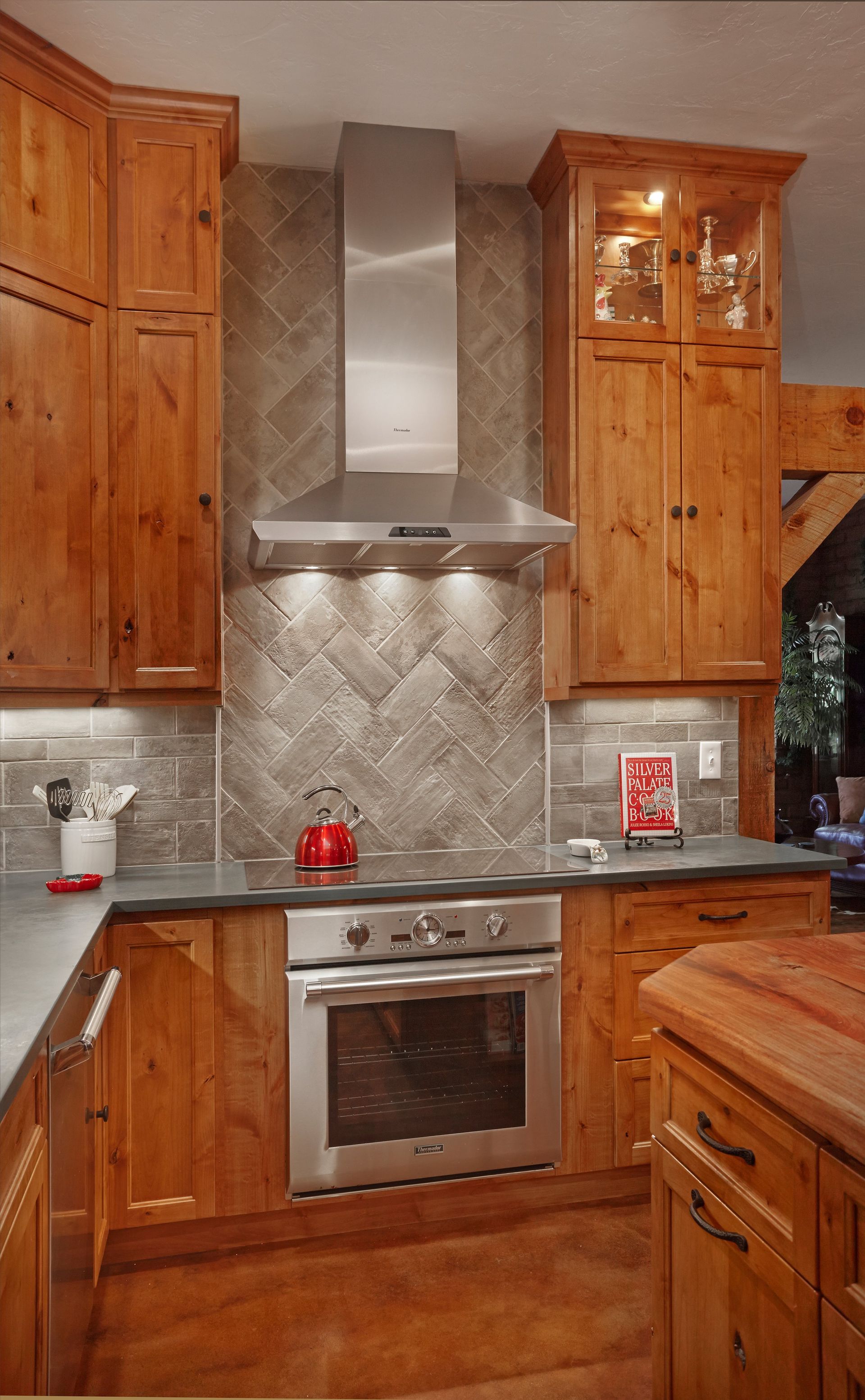 Kitchen with light wood cabinets, stainless steel oven and range hood, and gray tiled backsplash.