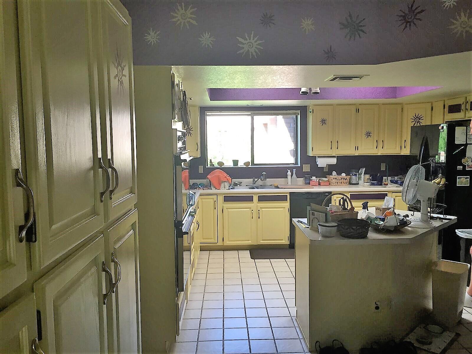 Yellow kitchen with cabinets, island, and window. Purple ceiling with snowflake decor.