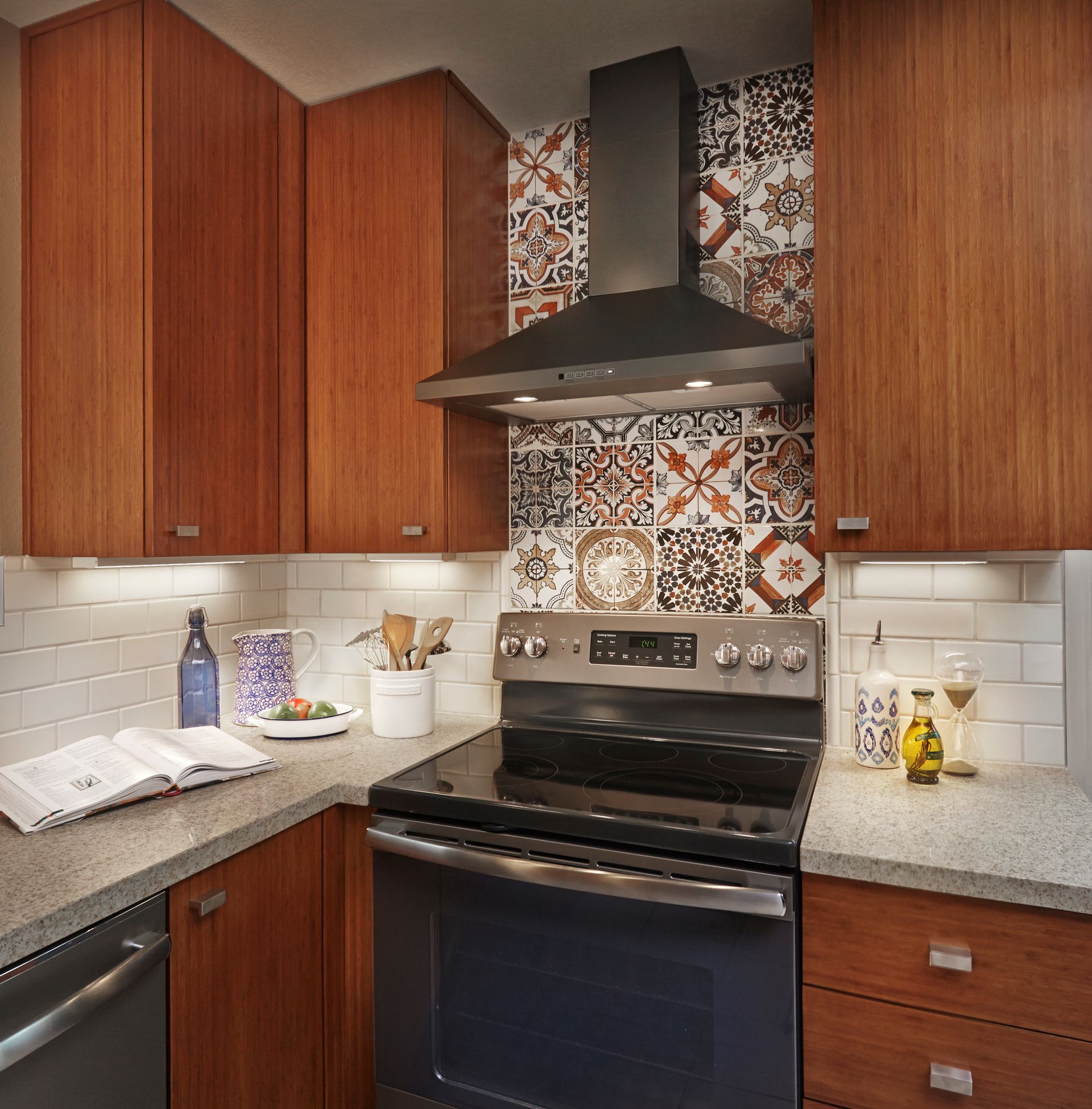 Kitchen with wooden cabinets, patterned backsplash, range, and countertop with accessories.