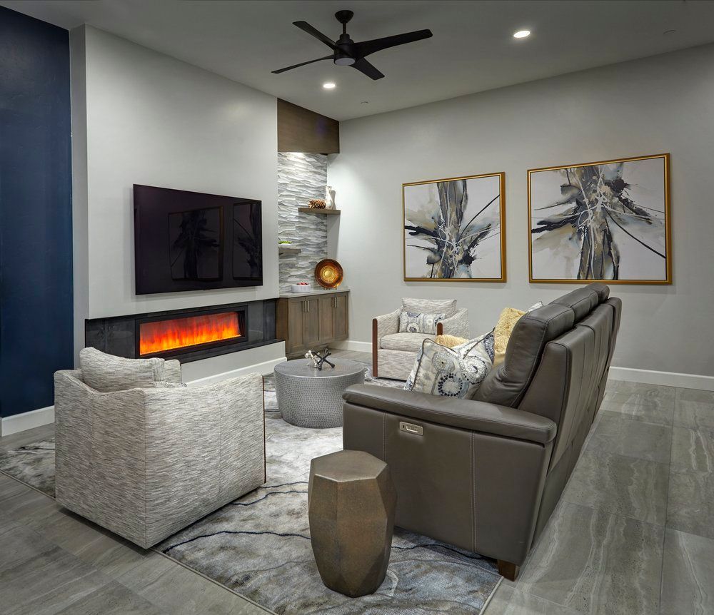 Modern living room with fireplace, TV, and gray furniture. Art, rug, and dark blue accent wall.