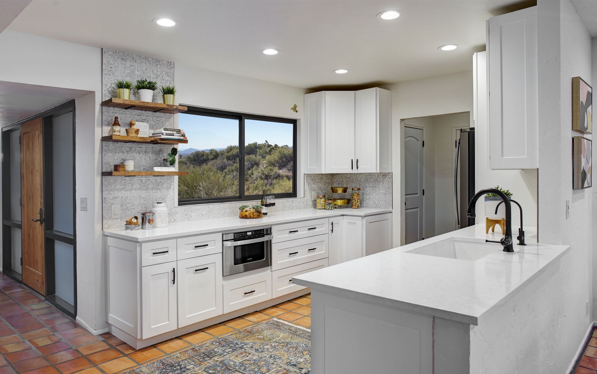White kitchen with open shelving, window view, and a small island with a sink.