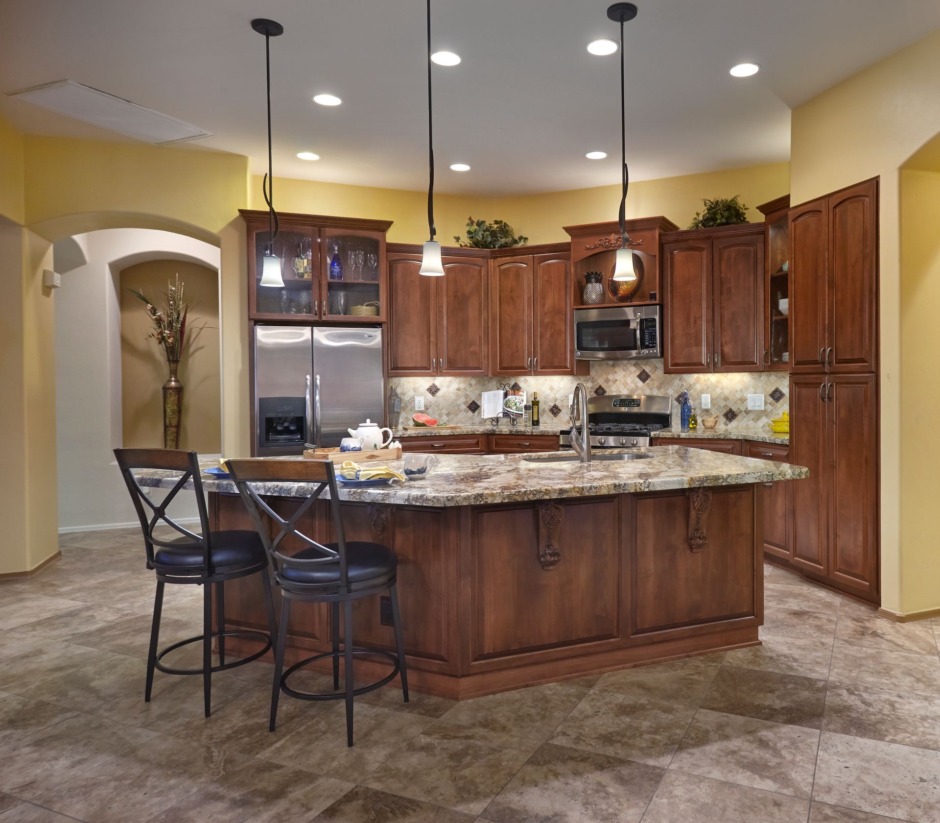 Kitchen with wood cabinetry, island with granite countertop, stainless steel appliances, and tile floor.