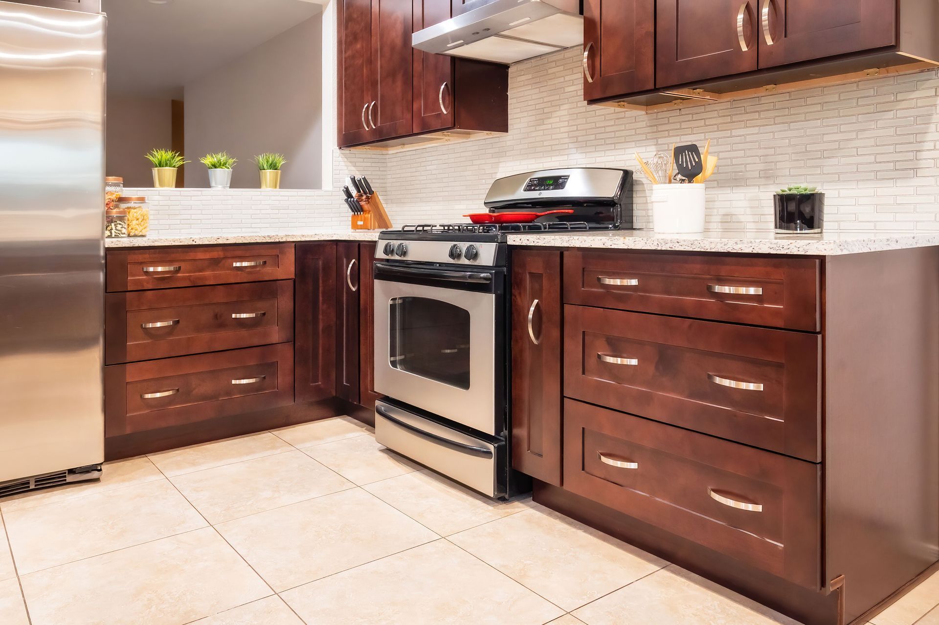 A kitchen with dark wood cabinets, stainless steel appliances, and beige countertops and backsplash.