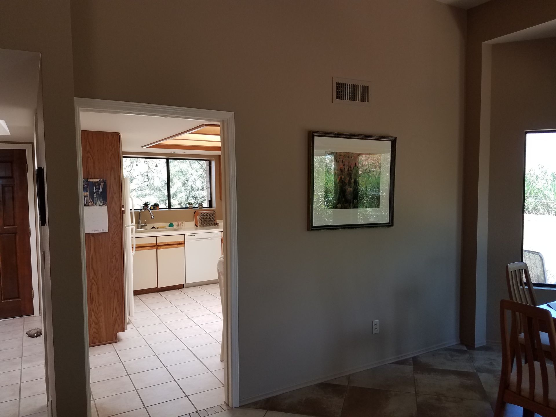 Interior view of a home showing an open doorway to the kitchen with beige walls and a framed picture.