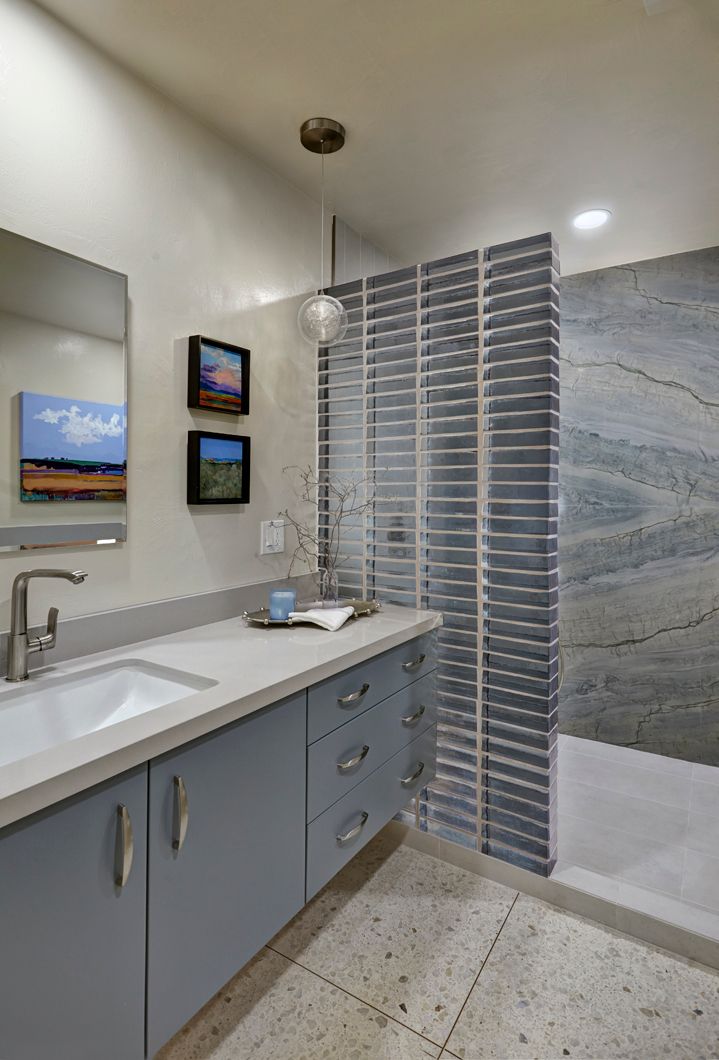 Bathroom with blue vanity, textured walls, glass tile shower, and colorful artwork.