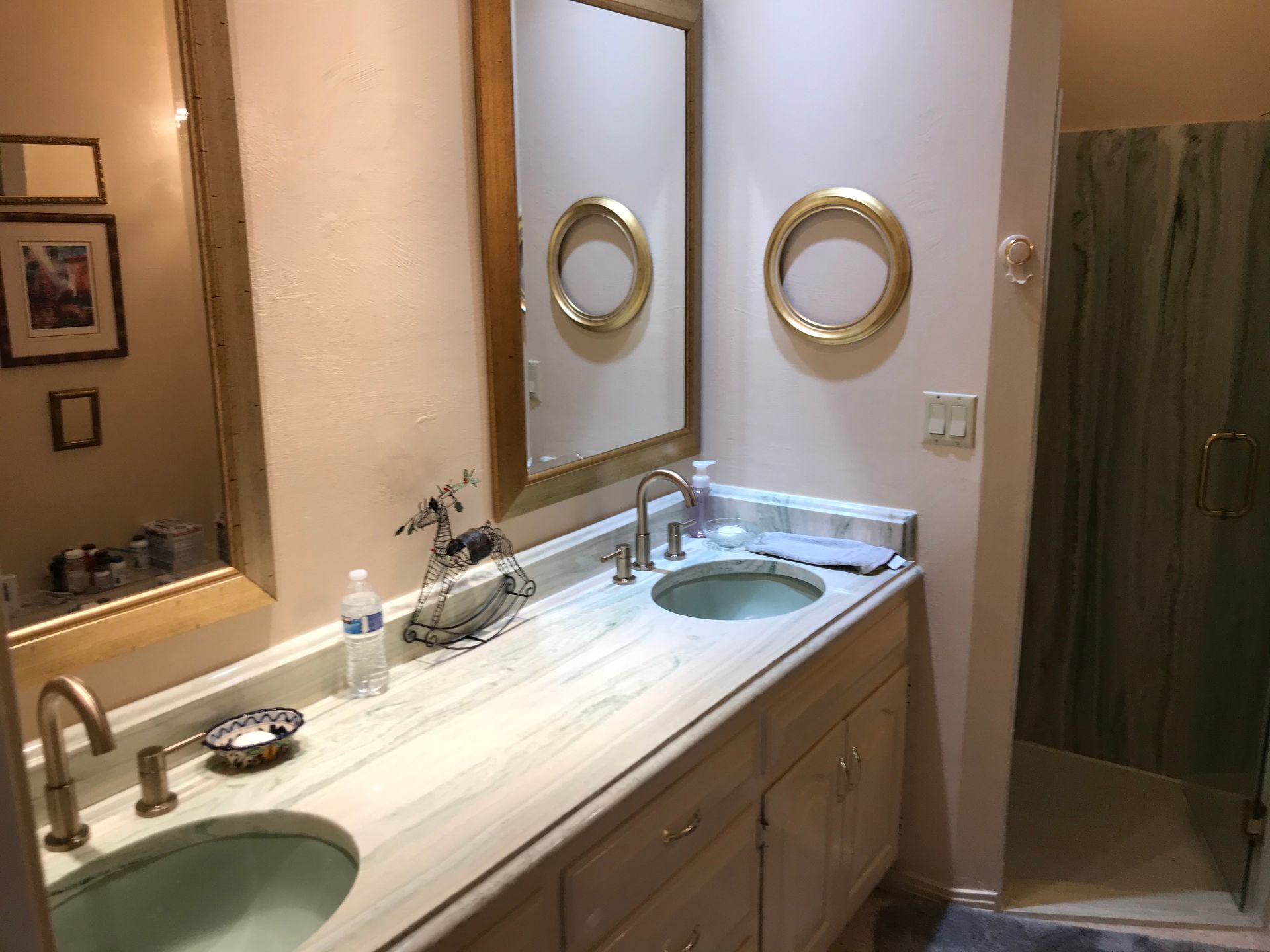 Bathroom with double sinks, mirror, gold frames, and a glass shower with green curtain.