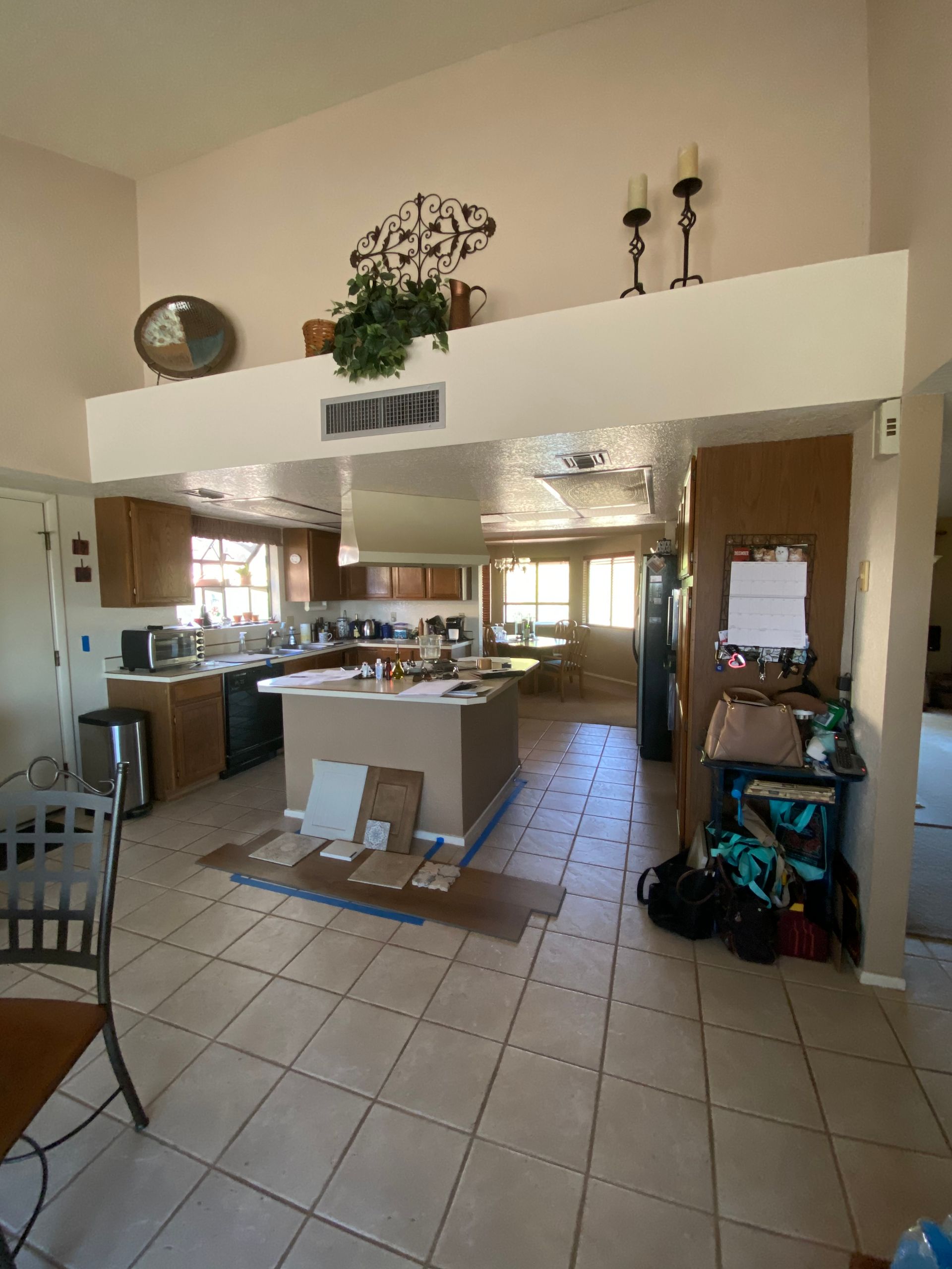 Kitchen interior with tile floor, cabinets, island, and high ceiling, open to dining area.