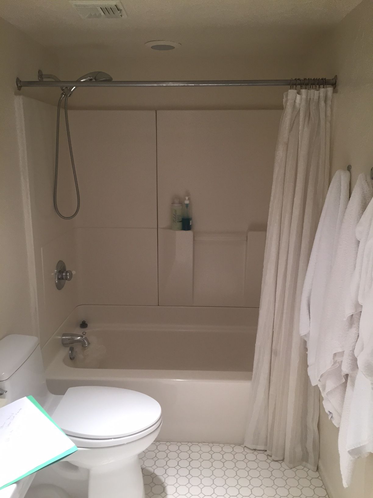 Bathroom with toilet, shower/tub combo, and white robes hanging on wall.