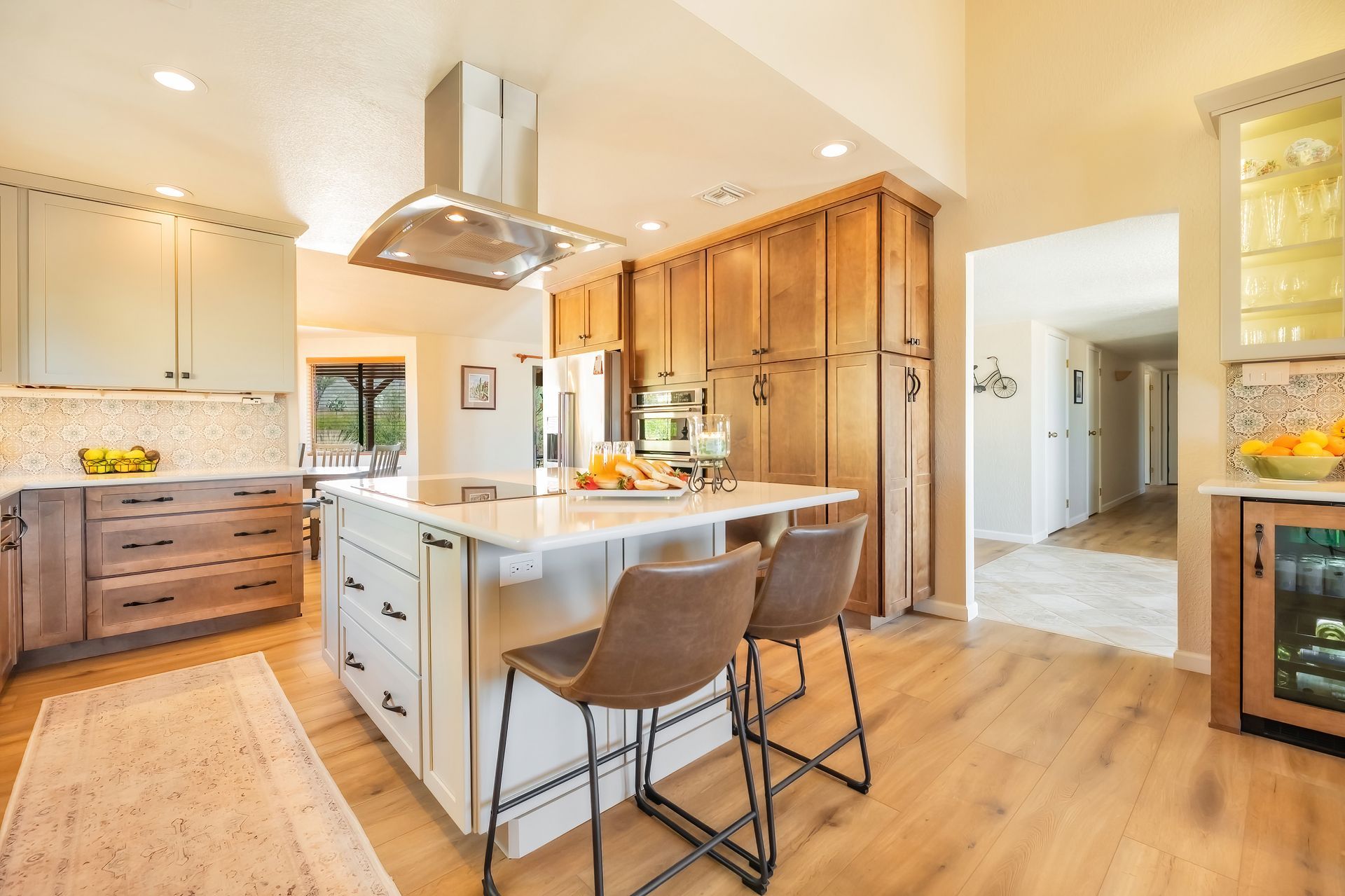 Modern kitchen with island, stainless steel range hood, wooden cabinets, and bar stools.