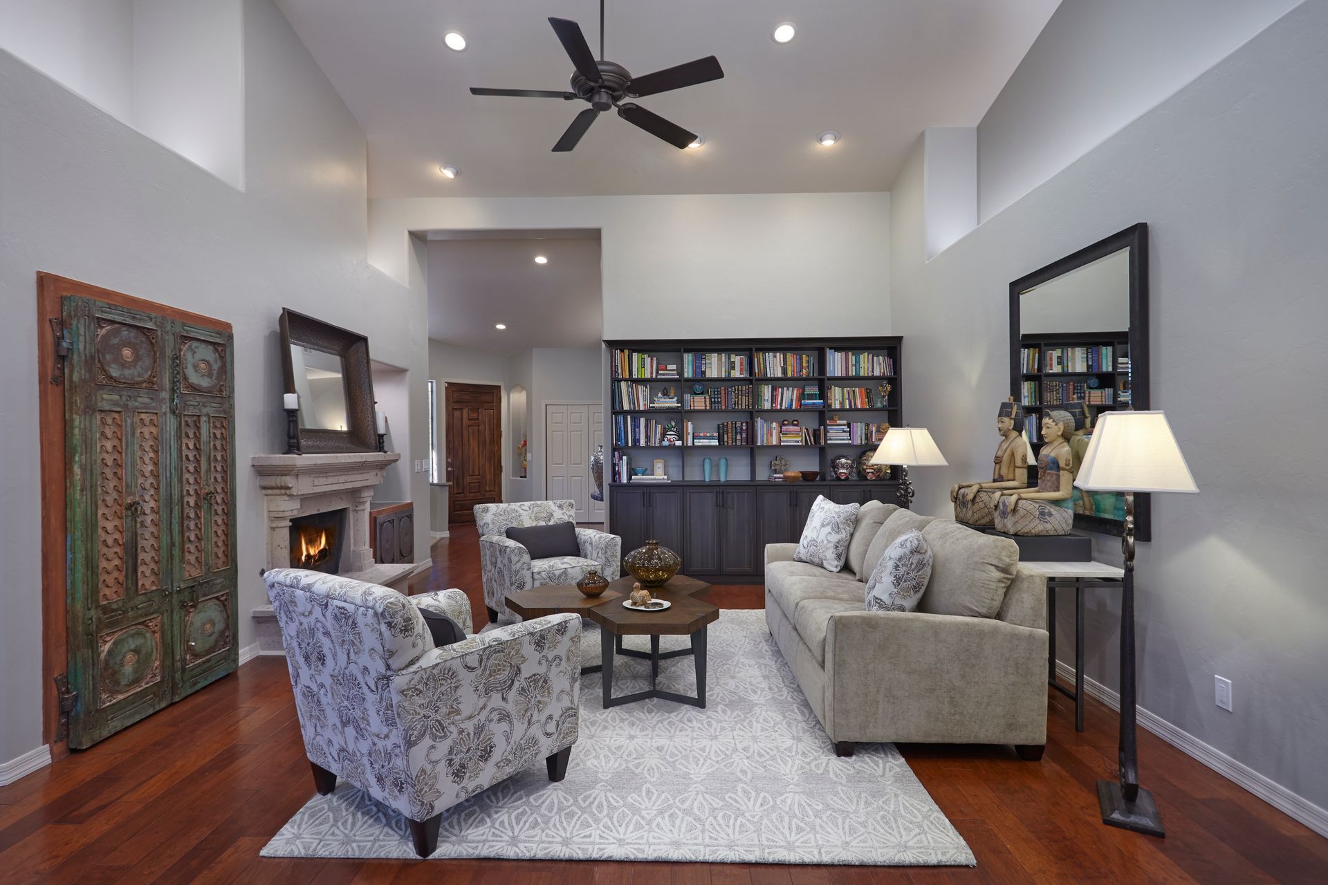 Living room with a fireplace, bookshelves, and various seating, with hardwood floors and light gray walls.