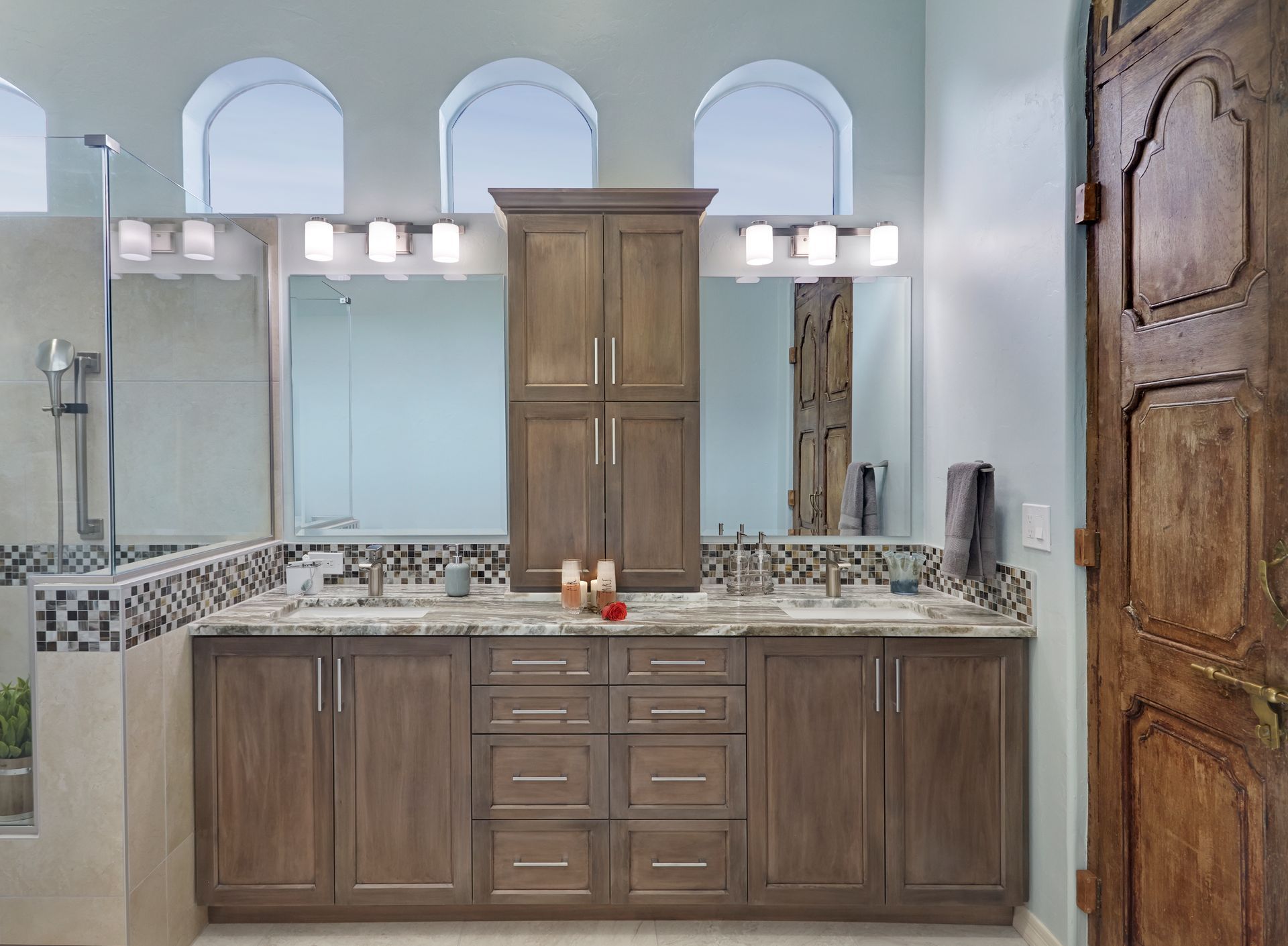 Bathroom with wood cabinets, double sinks, tall cabinet, and arched windows.