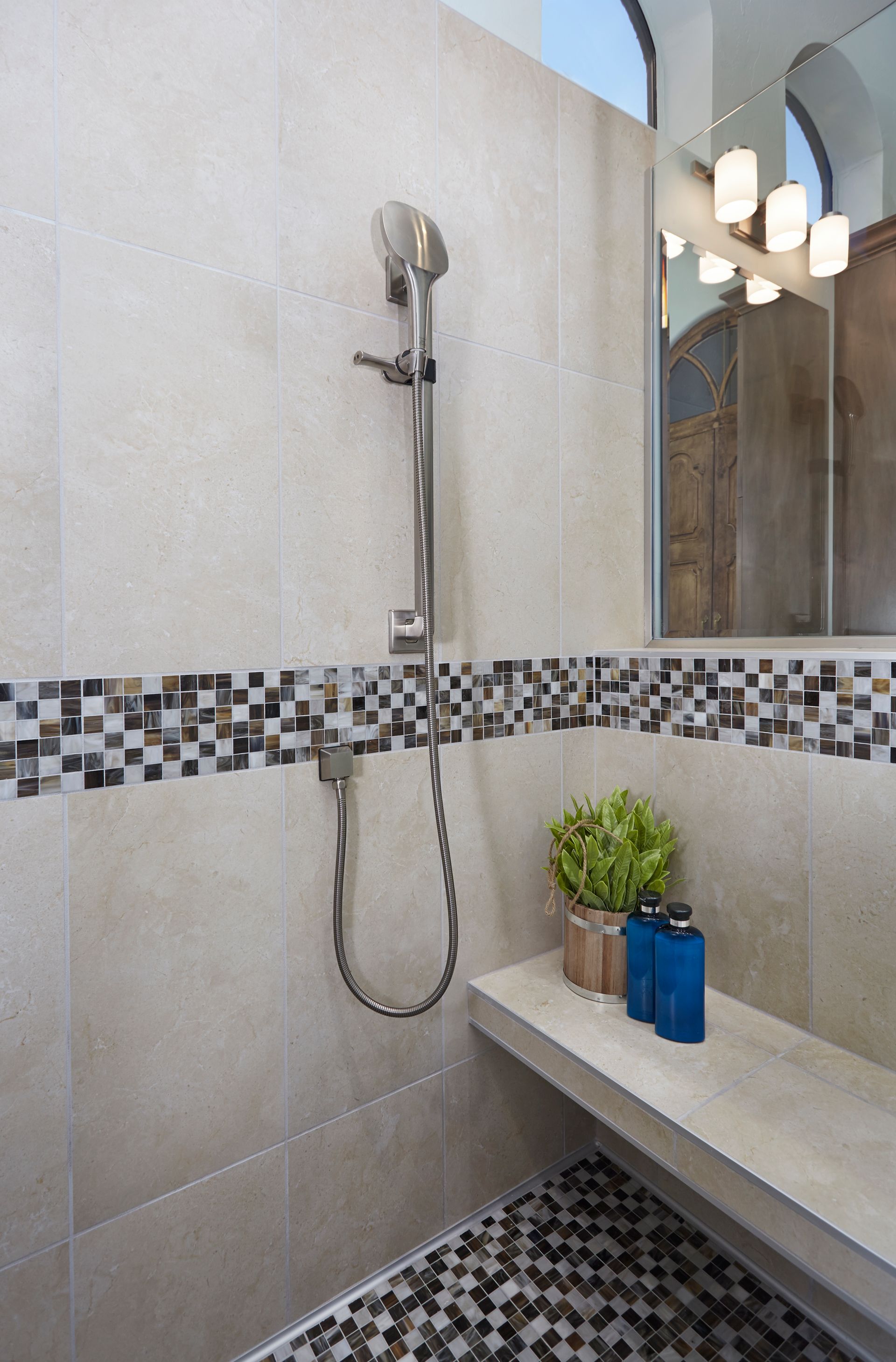 Shower with beige tile walls, mosaic tile border, pebble floor, and a built-in bench.