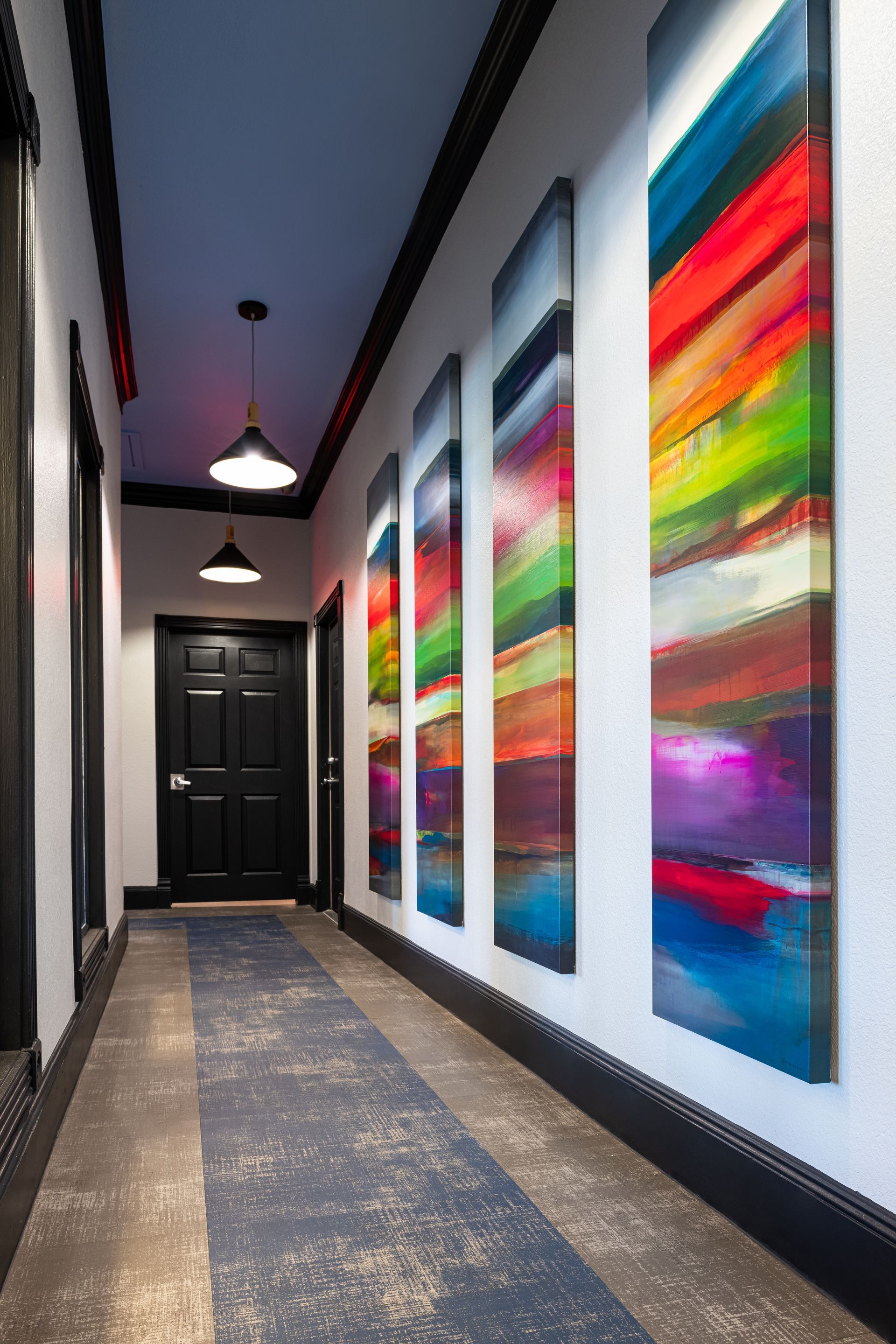 Hallway with colorful abstract art, black door, pendant lights, and patterned flooring.