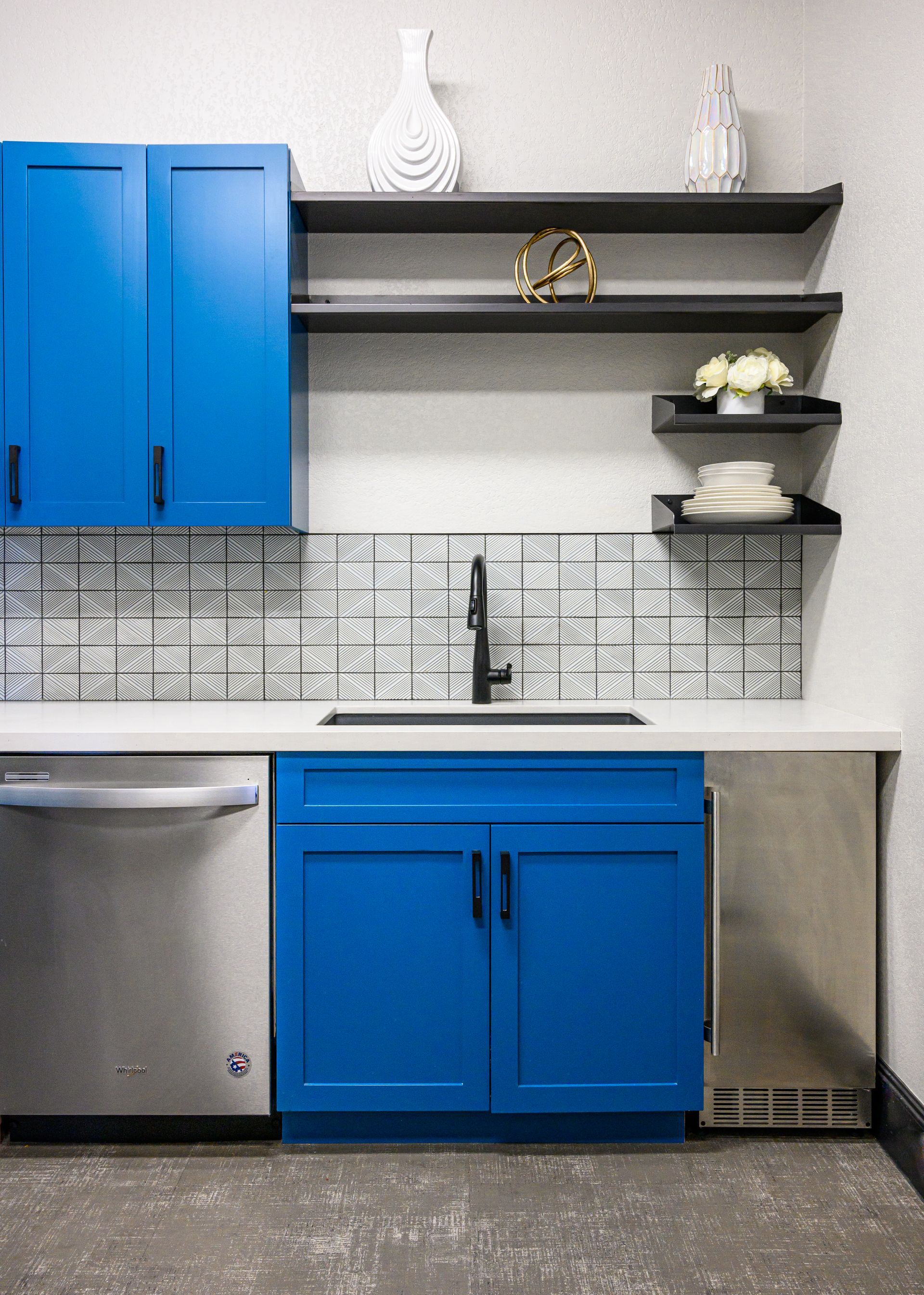 Blue and white kitchen with stainless steel appliances, black shelves, and decorative items.