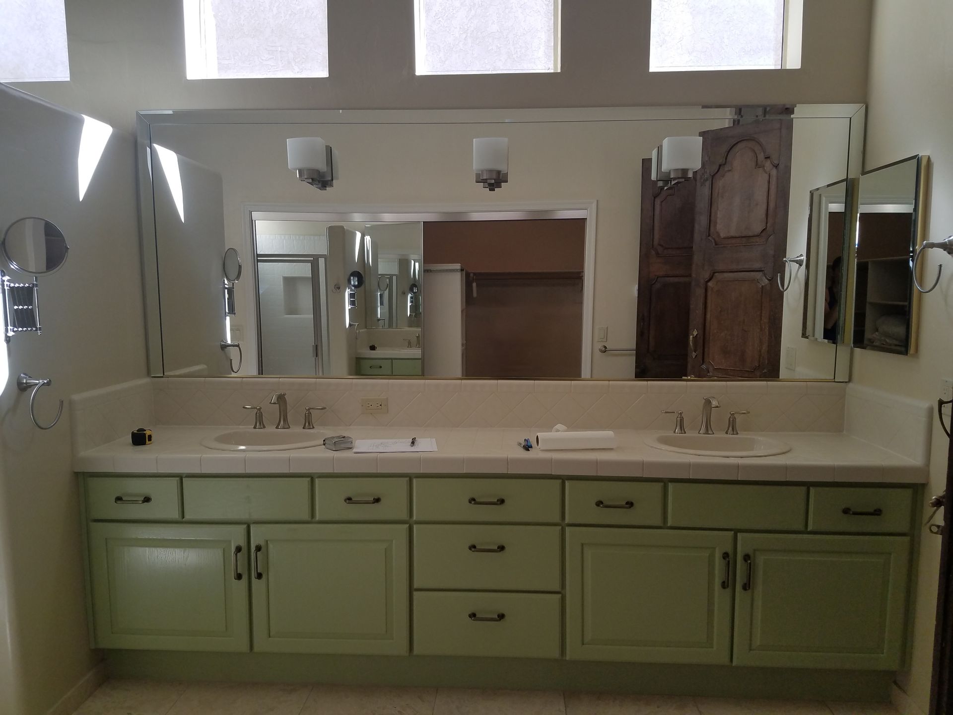 Bathroom with green cabinets, white counter, large mirror, and three sconces.