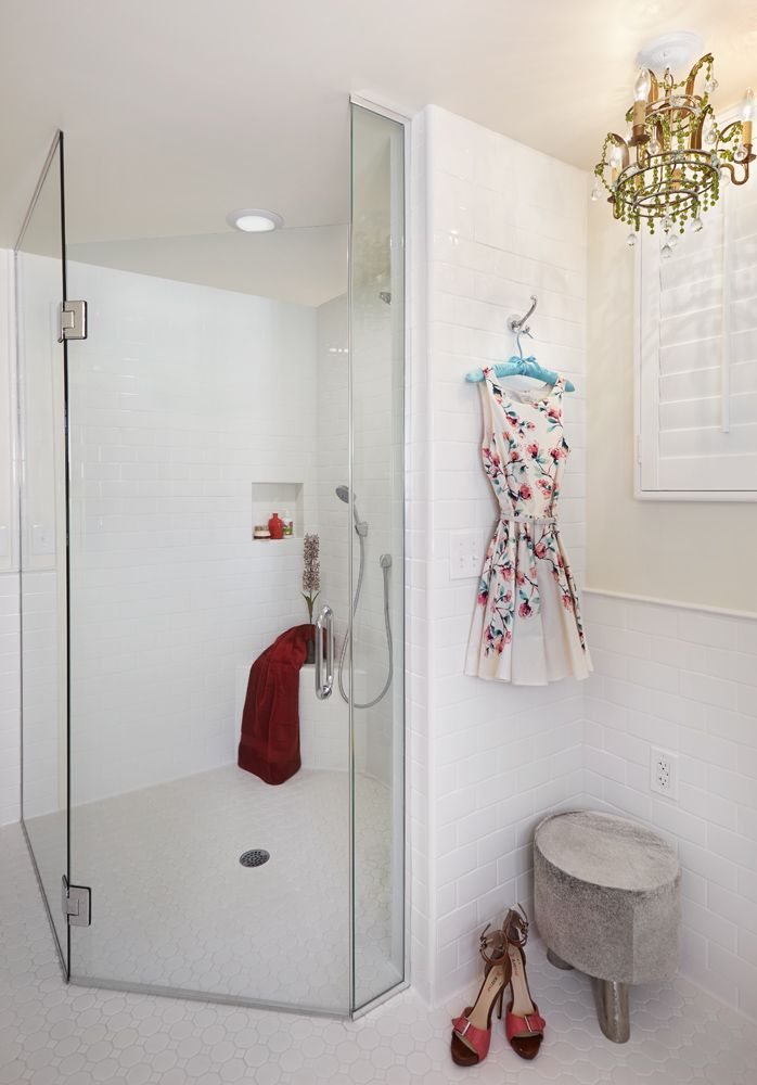 Modern white shower with glass doors, a red towel, and a floral dress hanging nearby.