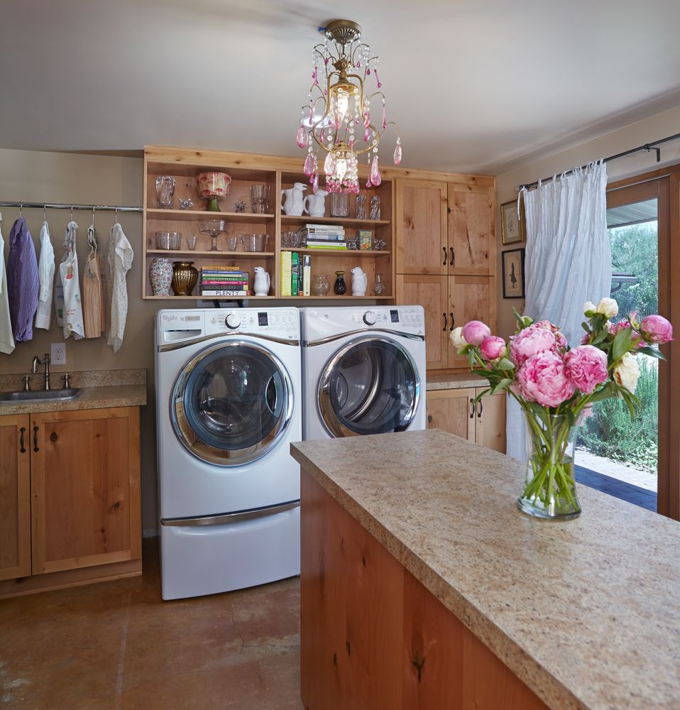 Laundry room with washer, dryer, wooden cabinets, countertop, clothes rack, flowers, and chandelier.
