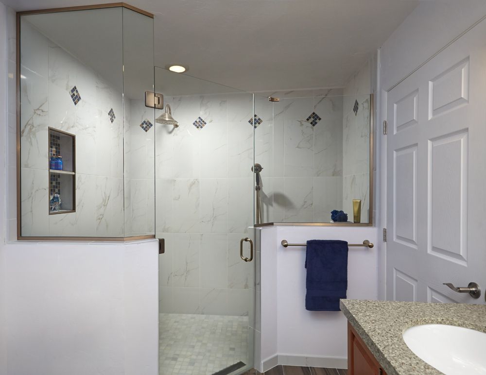 Bathroom with glass shower, white walls, granite countertop, towel rack with blue towel, and white door.