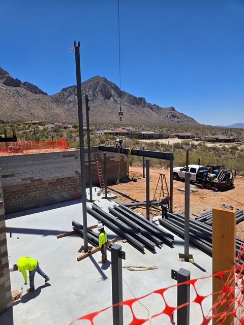 Construction site with metal beams, workers, and a mountain backdrop on a sunny day.
