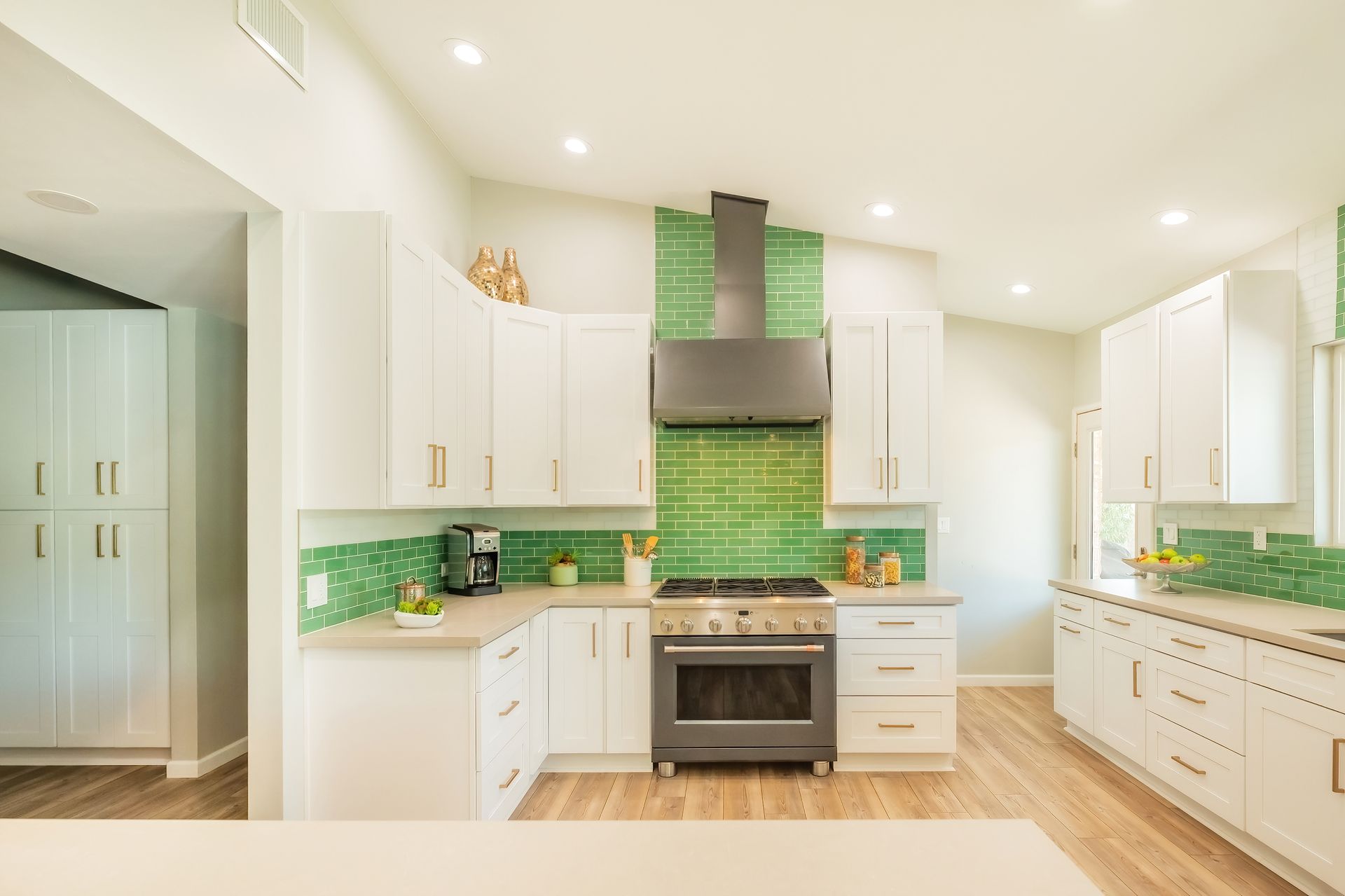 Bright kitchen with white cabinets, green backsplash, stainless steel appliances, and wood floors.