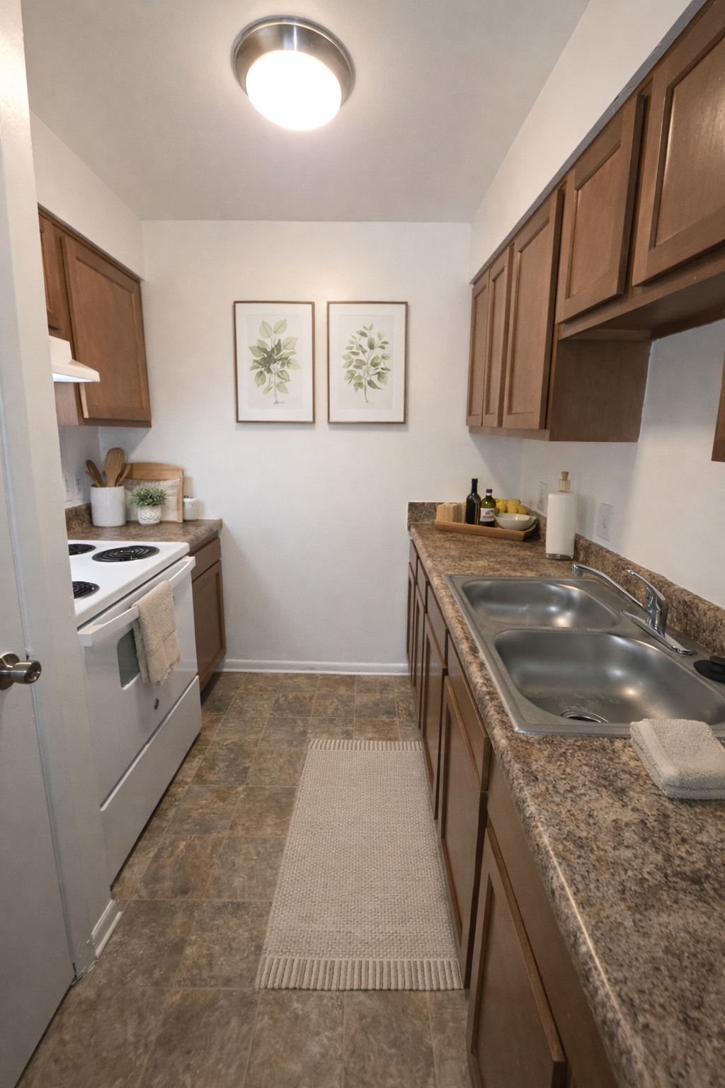 Narrow galley kitchen with wood cabinets, granite counters, white appliances, and framed wall art.