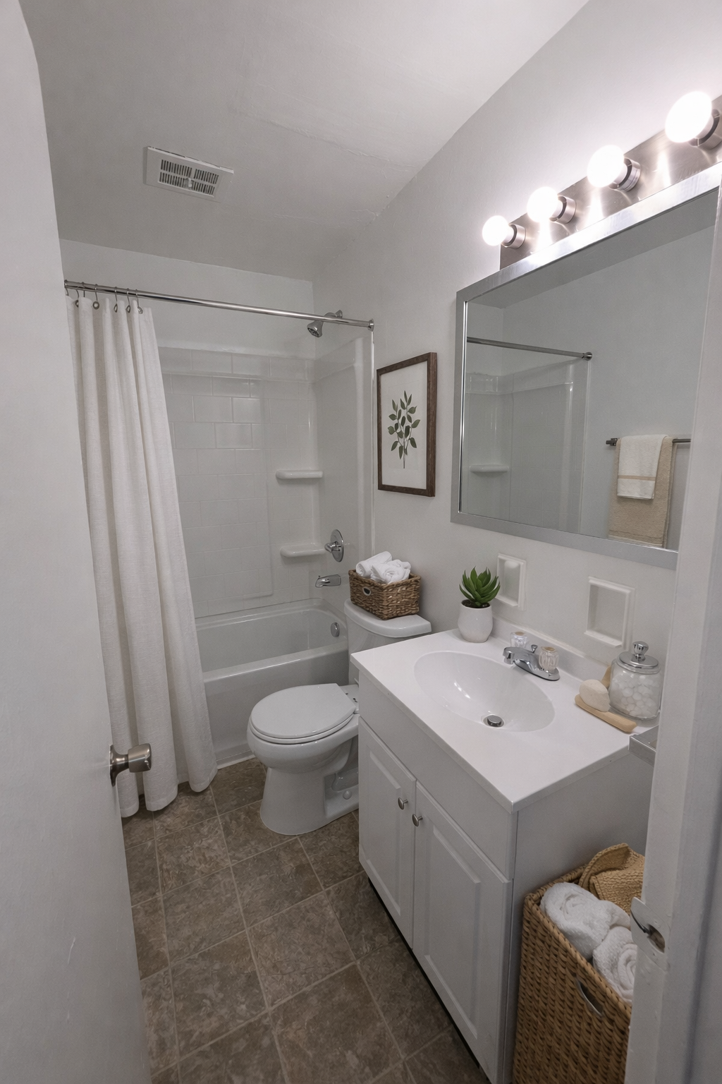 Bright white bathroom with shower curtain, toilet, vanity sink, mirror, and wicker laundry basket.