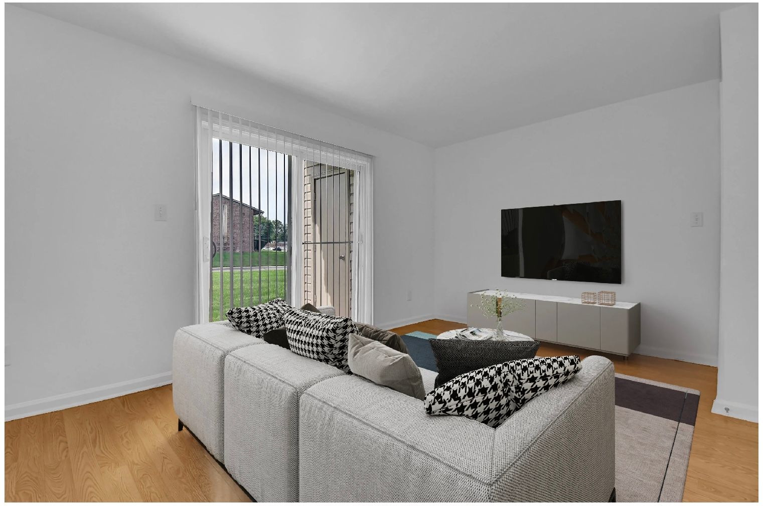Modern living room with gray sofa, wall-mounted TV, and sliding glass doors to a garden