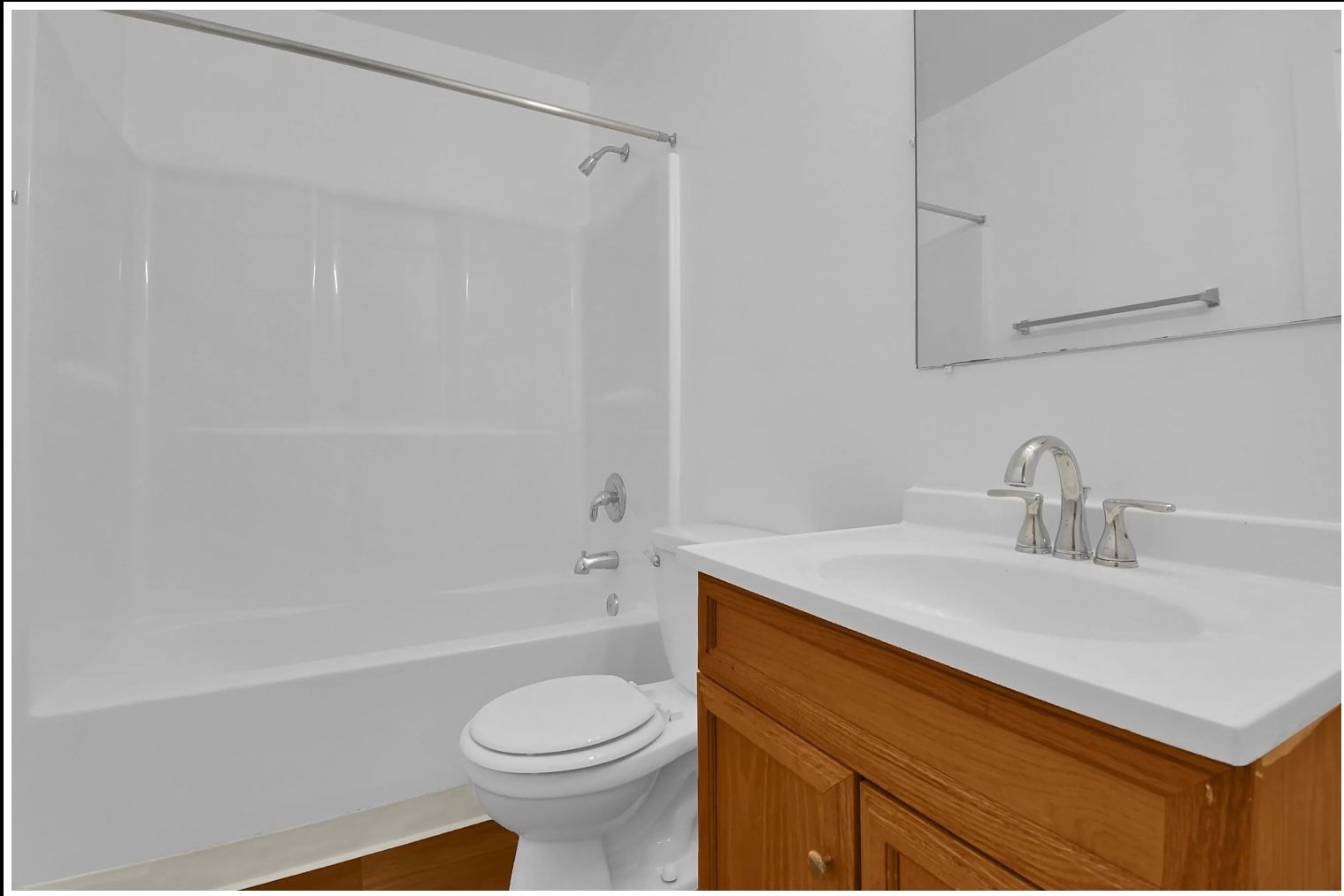 Small bathroom with a white bathtub, toilet, and wood vanity with sink and mirror.