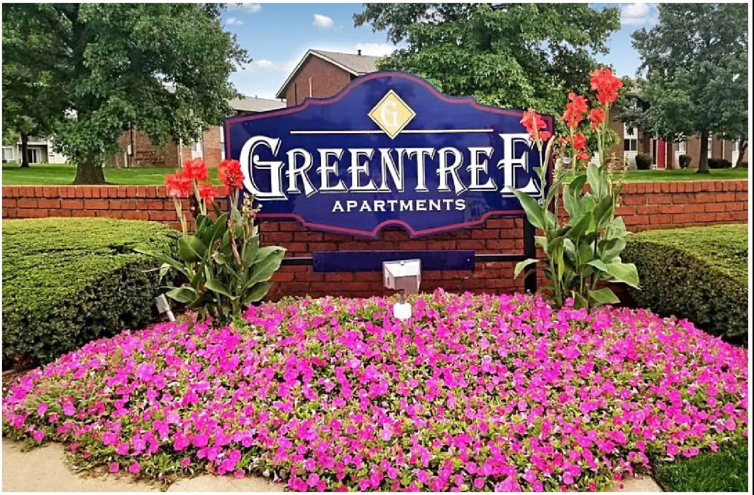 Greentree Apartments sign surrounded by pink flowers and greenery in a landscaped entrance