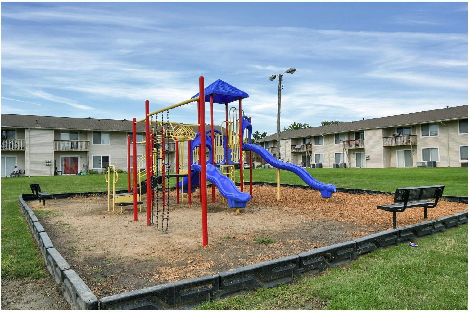 Playground with blue slides and red climbing bars in a grassy apartment courtyard
