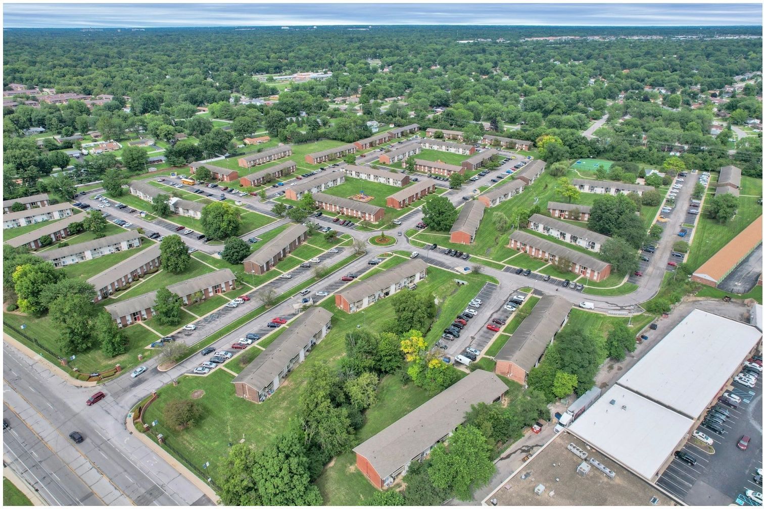 Aerial view of a suburban neighborhood with rows of houses, tree-lined streets, and a large building