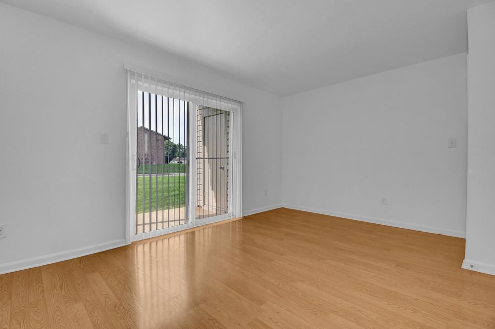Empty room with wood floors and sliding glass doors opening to a small patio and lawn.