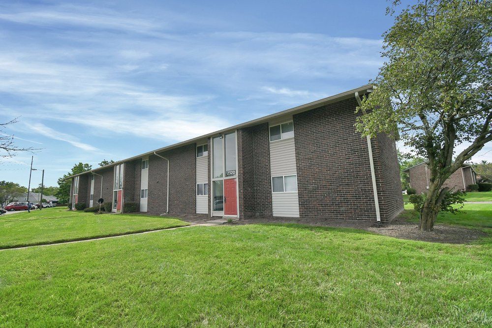Low-rise apartment building with red doors and green lawn under a blue sky