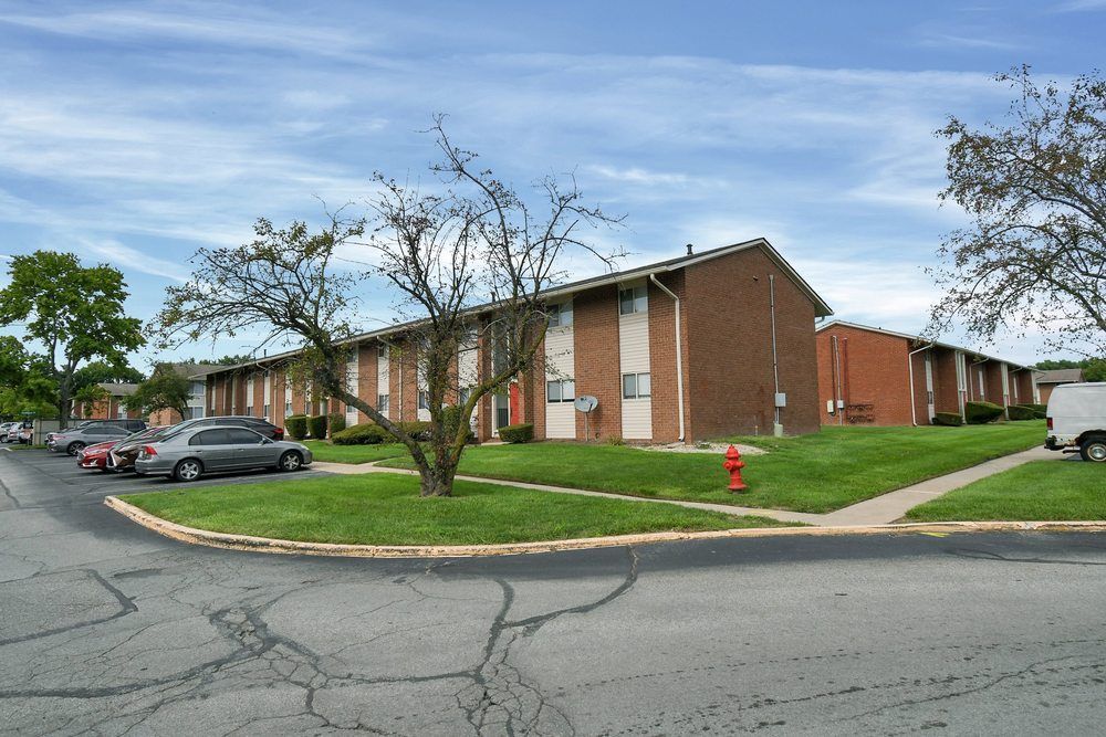 Suburban brick apartment building with parked cars, a red fire hydrant, and leafless trees by a street curve