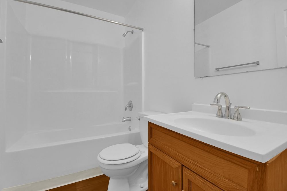 Clean white bathroom with tub, toilet, and wood vanity with sink and mirror