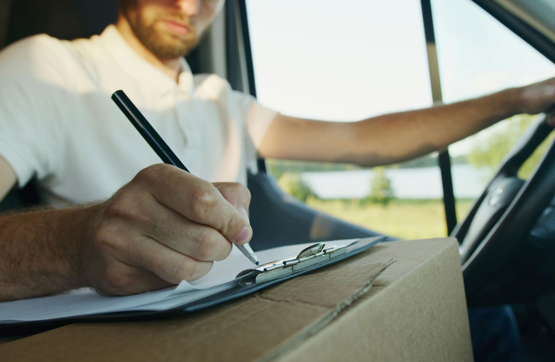 Le livreur signe des documents sur un bloc-notes, assis dans sa camionnette avec un colis.