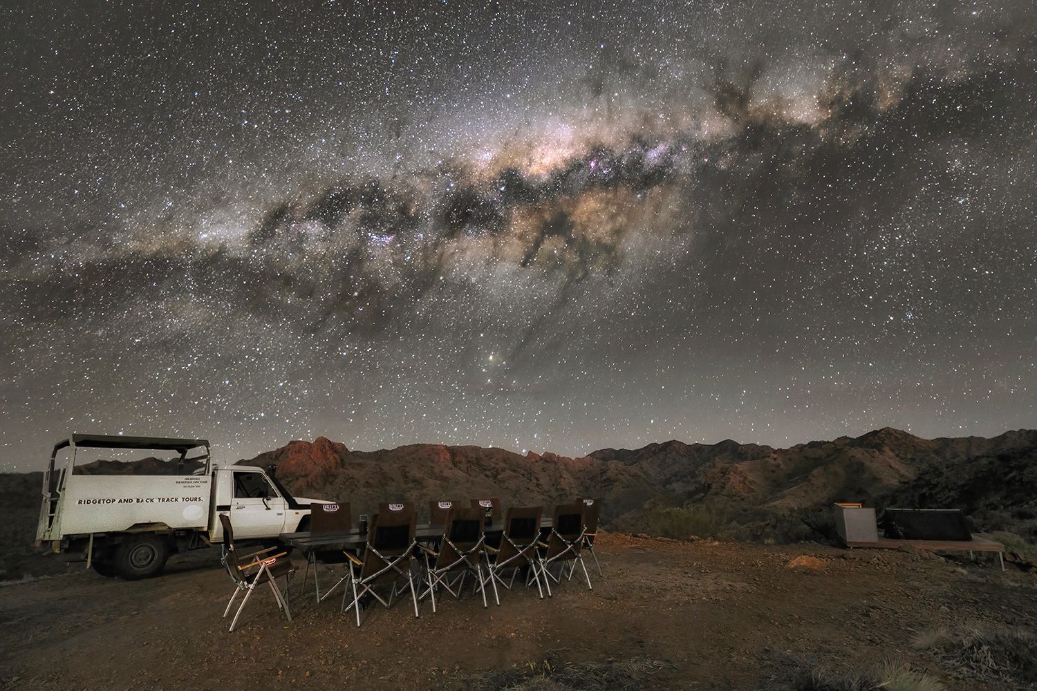 Outdoor dining set up of the Ridgetop Sleepout Experience under the starry night sky at Arkaroola, ready for a stargazing experience in an International Dark Sky Sanctuary, showcasing the Milky Way in all its glory. Experience this on the Arkaroola Photography Tour.