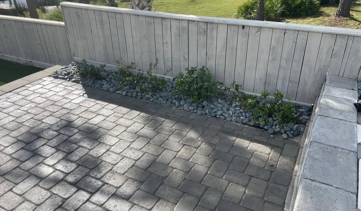 Patio with gray pavers, a stone bed, plants, and a light wooden fence.