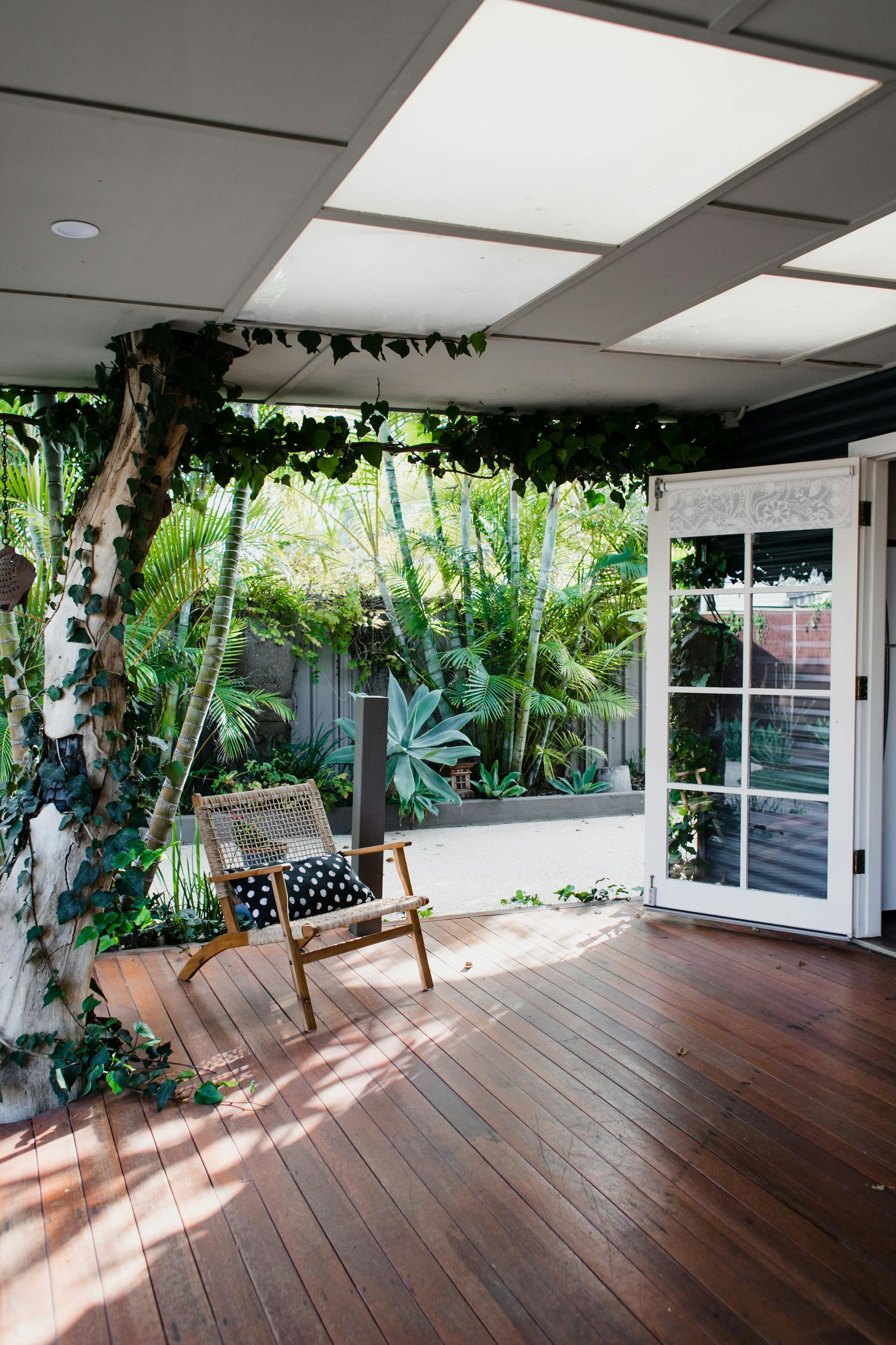 Wooden deck with chair, vines, and white-paneled doors, leading to a lush green garden.