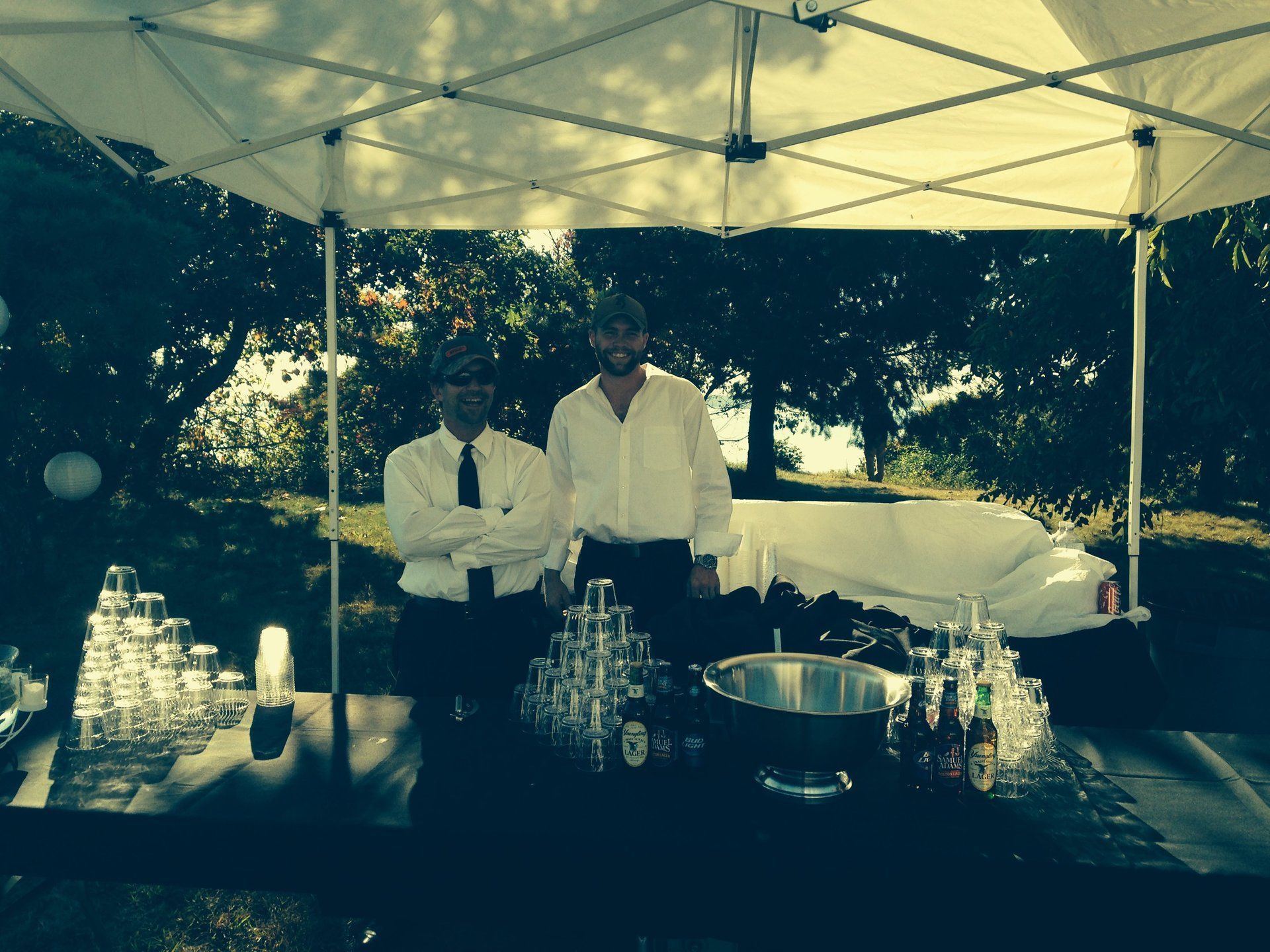 Two men standing in front of a bar with glasses and bottles